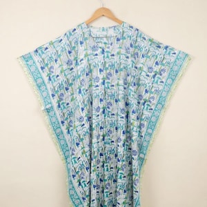 May include: A loose-fitting kaftan dress featuring a white base with a repeating pattern of blue and green floral and botanical motifs. The garment has wide, short sleeves, a V-neckline, and a decorative border along the edges and hemline.