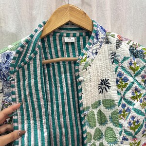 Pu&ograve; includere: Una giacca trapuntata bianca con una fodera a righe verde e bianca. La giacca ha una stampa floreale con fiori blu, verdi e bianchi. La giacca ha una chiusura con bottoni e un colletto. L'etichetta sulla giacca dice "S" e "Made in India".