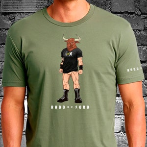 May include: A green t-shirt with a graphic of a bull-headed wrestler wearing black boots and a black t-shirt with the text "RABO DE ORO". The text "RABO DE ORO" is also printed on the bottom of the shirt.