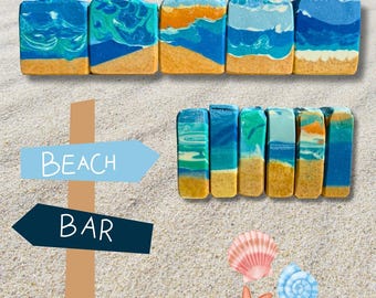 May include: Handmade soaps with a beach design. The soaps have blue, green, and orange patterns, mimicking waves over a sandy layer. The image also shows a sign that says "BEACH BAR", seashells, and a starfish.