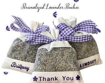 May include: Three white fabric lavender pouches with purple gingham ribbon bows. The pouches are filled with dried lavender and have personalized names: "Brittany", "Thank You", and "Lindsey".