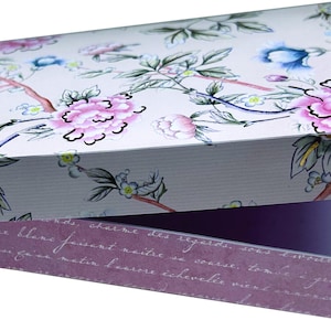 Könnte beinhalten: Eine rechteckige Geschenkbox mit floralem Design. Der Deckel zeigt rosa Pfingstrosen, blaue Akzente und grüne Blätter auf hellem Hintergrund. Der Innenraum der Box ist lila, und der Rand hat Schrifttext.