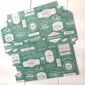 Puede incluir: Papel estampado en verde y blanco con varios dise&ntilde;os tem&aacute;ticos de mercado vintage. El papel presenta texto como "Boutique Market", "Vintage", "Antiques", "Happy Times", "Amazing Vintage", "Genuine Memories", "Must See Vintage Boutique Market", "Collectibles", "Memorabilia", y "Classic Vintage".