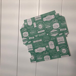 Puede incluir: Papel estampado verde y blanco con un tema de mercado vintage. El papel presenta varias etiquetas y dise&ntilde;os con palabras como "Vintage", "Mercado", "Antig&uuml;edades" y "Recuerdos".
