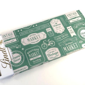 Puede incluir: Un papel de regalo verde y blanco con un tema de mercado vintage. El papel presenta una bicicleta, texto que dice "Boutique Market" y las palabras "Classic Vintage".