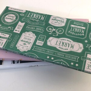 Puede incluir: Una caja de regalo verde y blanca con un tema de mercado vintage. La caja est&aacute; decorada con un patr&oacute;n repetitivo de etiquetas y texto que dice "Boutique Market", "Antique Market", "Rare Finds", "Vintage", "Classic Vintage", "Welcome", "Legacy", "Happy Times", "Collectibles", "Memorabilia" y "Since 1983".