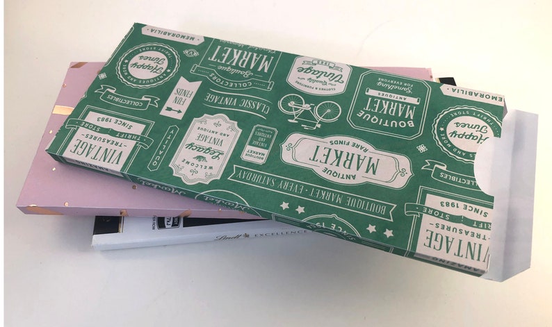 Puede incluir: Una caja de regalo verde y blanca con un tema de mercado vintage. La caja est&aacute; decorada con un patr&oacute;n repetitivo de etiquetas y texto que dice "Boutique Market", "Antique Market", "Rare Finds", "Vintage", "Classic Vintage", "Welcome", "Legacy", "Happy Times", "Collectibles", "Memorabilia" y "Since 1983".