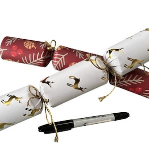 May include: Christmas crackers with gold deer and festive patterns. The crackers are white and red with gold accents, tied with twine. A black Sharpie marker is included for scale.