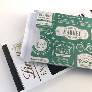 Puede incluir: Una bolsa de regalo de papel verde y blanca con un tema de mercado vintage. La bolsa presenta un patr&oacute;n repetido de varios logotipos y texto, incluyendo "Boutique Market", "Antique Market", "Happy Times" y "Vintage".