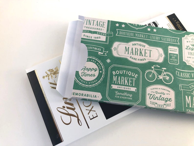 Puede incluir: Una bolsa de regalo de papel verde y blanca con un tema de mercado vintage. La bolsa presenta un patr&oacute;n repetido de varios logotipos y texto, incluyendo "Boutique Market", "Antique Market", "Happy Times" y "Vintage".