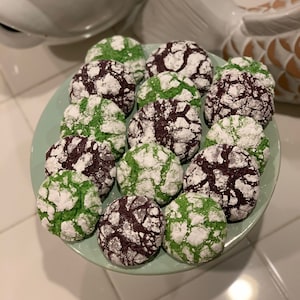 May include: A plate of green and purple cookies with powdered sugar on top. The cookies are arranged in a circle on a light green plate.