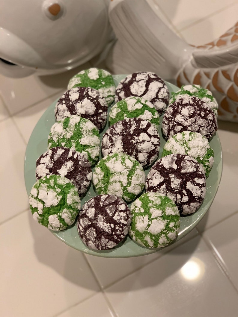 May include: A plate of green and purple cookies with powdered sugar on top. The cookies are arranged in a circle on a light green plate.
