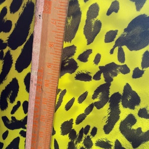 Puede incluir: Primer plano de una tela amarilla con un estampado de leopardo negro. Una regla de madera se coloca sobre la tela para mostrar la escala.
