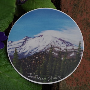 May include: A round sticker with a photo of a snow-capped mountain peak with a blue sky and white clouds. The sticker has the text "SeaGreen Studios" at the bottom.