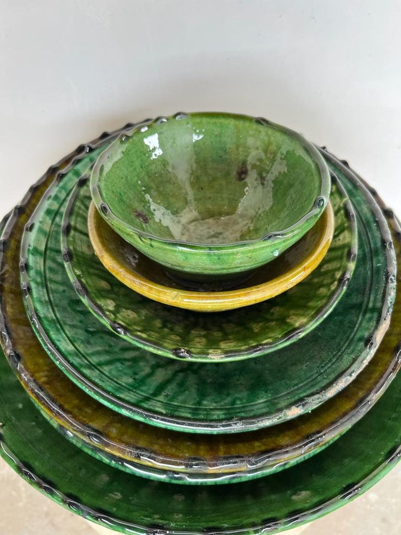 May include: A stack of five glazed ceramic dishes consisting of four round plates and one small bowl. The pieces feature a glossy finish in shades of deep forest green and mustard yellow, with dark, scalloped, and textured edges on each item.