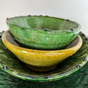May include: A stack of three ceramic bowls with a glossy finish. The top bowl is vibrant green, the middle bowl is a warm mustard yellow, and the bottom bowl is a deep forest green. Each bowl features a scalloped, textured rim and a smooth interior.