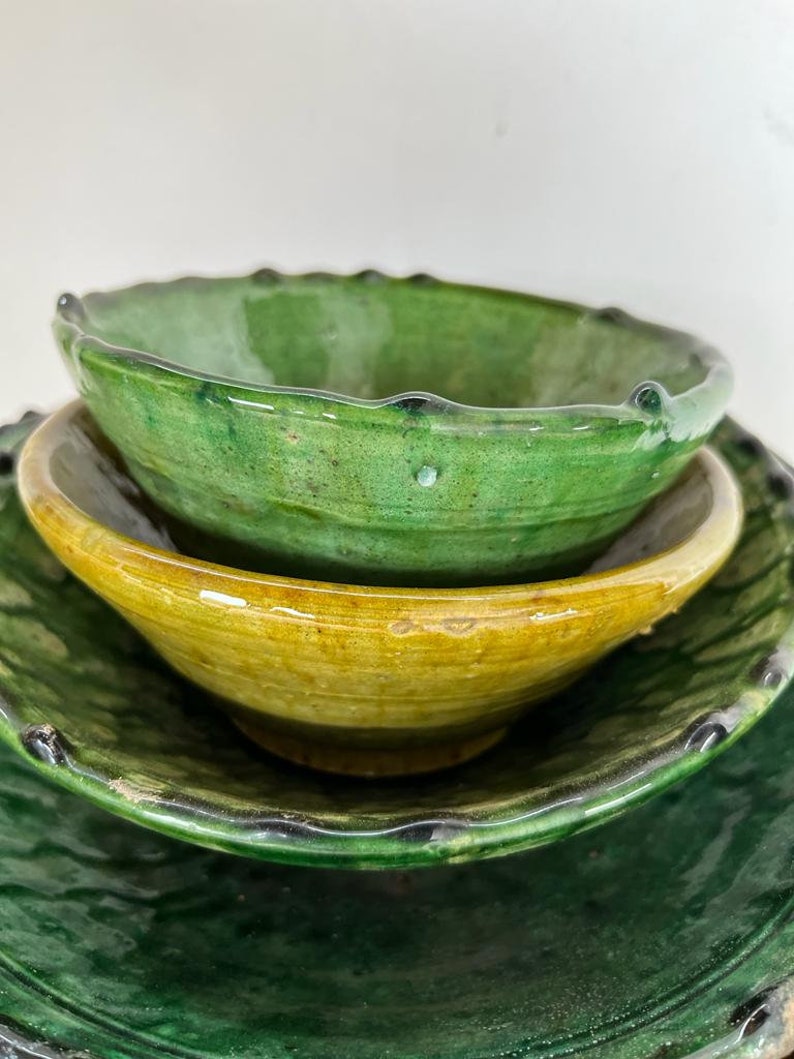 May include: A stack of three ceramic bowls with a glossy finish. The top bowl is vibrant green, the middle bowl is a warm mustard yellow, and the bottom bowl is a deep forest green. Each bowl features a scalloped, textured rim and a smooth interior.