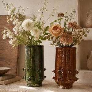 Peut inclure: Deux vases cylindriques en céramique avec une finition brillante et des détails en forme de pointes saillantes. Un vase est vert forêt profond et l'autre est d'un brun terreux riche. Chaque vase contient un bouquet de fleurs fraîches.