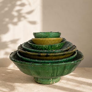 May include: A stack of six nested ceramic bowls with a glossy glaze in shades of emerald green and olive yellow. Each bowl features a wide, shallow basin, a pedestal base, and a decorative scalloped rim with small, raised bumps along the edge.