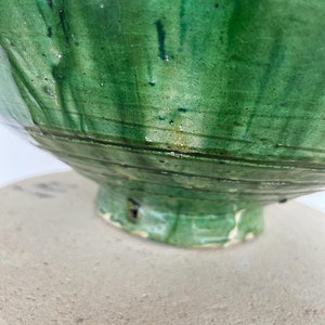 May include: A ceramic bowl with a vibrant green glaze featuring a visible crackle pattern and dark green vertical drip marks. The bowl has a rounded body with horizontal incised lines circling the base and a flared foot with a small dark chip.