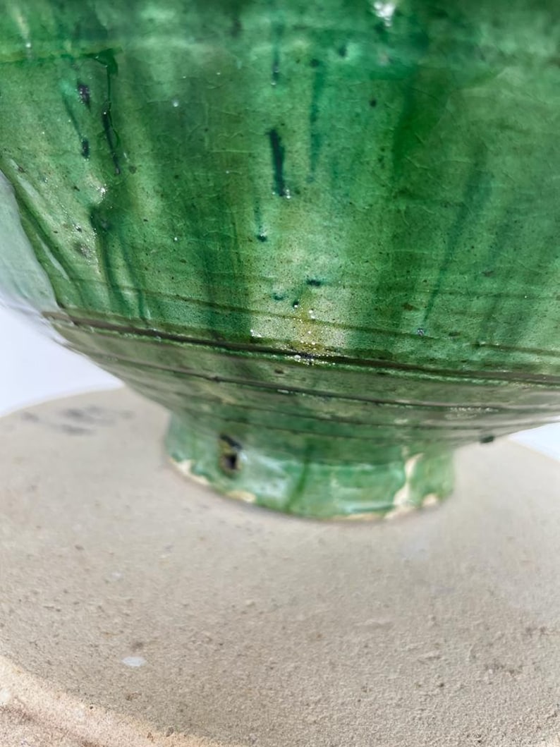 May include: A ceramic bowl with a vibrant green glaze featuring a visible crackle pattern and dark green vertical drip marks. The bowl has a rounded body with horizontal incised lines circling the base and a flared foot with a small dark chip.