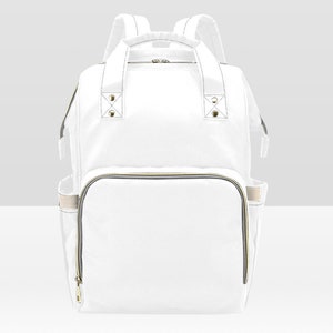 May include: A white canvas diaper bag backpack with gold zippers and accents. The bag has a large main compartment and several smaller pockets.