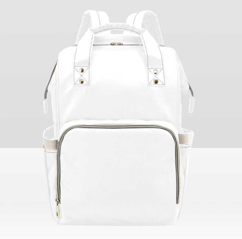 May include: A white canvas diaper bag backpack with gold zippers and accents. The bag has a large main compartment and several smaller pockets.