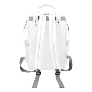 May include: White canvas backpack with gray adjustable straps and a zipper closure. The backpack has two side pockets and a small pocket on the front.