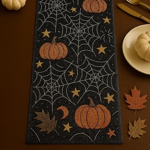 Op de afbeelding: Zwarte Halloween tafelloper met een spinnenwebontwerp, oranje pompoenen en gouden sterren. De loper is versierd met een halve maan en herfstbladeren. Een brandende kaars, witte pompoenen en servies staan op de tafel.