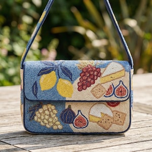 Puede incluir: Bolso de cuentas con fondo azul y cierre de solapa. El bolso presenta diseños de cuentas de limones, uvas, higos, queso y galletas. El bolso tiene una correa azul.
