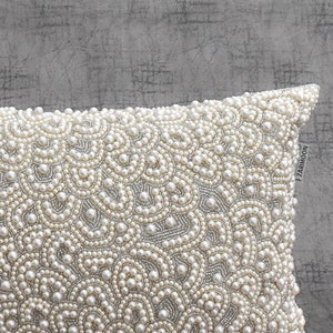 Puede incluir: Una almohada blanca con un dise&ntilde;o de cuentas de imitaci&oacute;n de perlas. La almohada est&aacute; decorada con un patr&oacute;n repetitivo de peque&ntilde;as cuentas redondas.