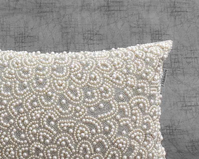 Puede incluir: Una almohada blanca con un dise&ntilde;o de cuentas de imitaci&oacute;n de perlas. La almohada est&aacute; decorada con un patr&oacute;n repetitivo de peque&ntilde;as cuentas redondas.