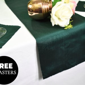 Op de afbeelding: Een donkergroene tafelrunner met een witte roos en een koperkleurig object erop. De tekst "FREE COASTERS" staat in een zwarte cirkel op een witte achtergrond.