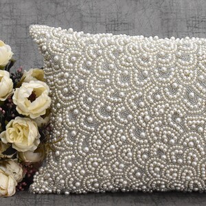 Puede incluir: Una almohada blanca con un dise&ntilde;o de perlas. La almohada est&aacute; cubierta de peque&ntilde;as perlas blancas que crean un patr&oacute;n de remolino.