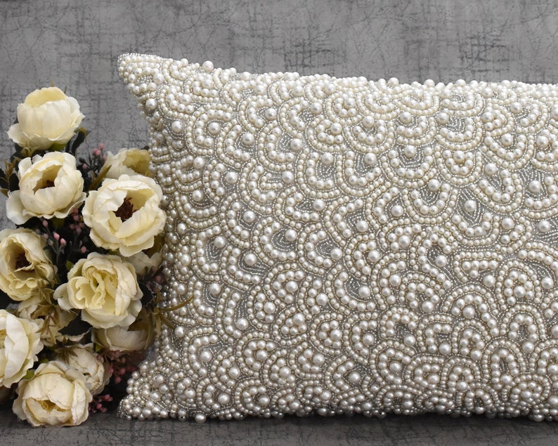 Puede incluir: Una almohada blanca con un dise&ntilde;o de perlas. La almohada est&aacute; cubierta de peque&ntilde;as perlas blancas que crean un patr&oacute;n de remolino.