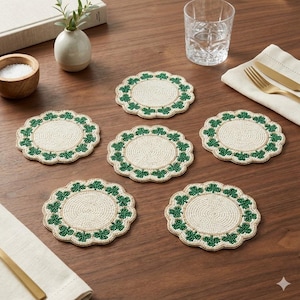 May include: Six round beaded coasters with a cream-colored center and a scalloped edge. The edge is decorated with green shamrock designs. The coasters are arranged on a wooden table, with a glass, a napkin, and a small bowl visible.
