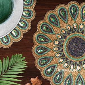 May include: A set of two round beaded placemats with a peacock feather design. The placemats are gold, green, and blue with a circular pattern of sequins. The placemats are on a wooden surface.