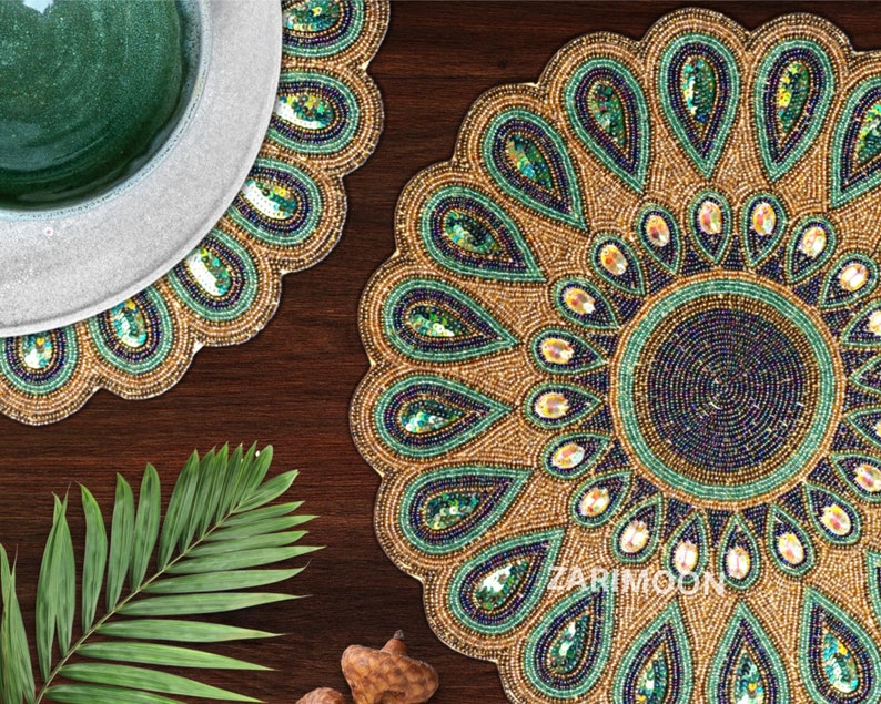 May include: A set of two round beaded placemats with a peacock feather design. The placemats are gold, green, and blue with a circular pattern of sequins. The placemats are on a wooden surface.