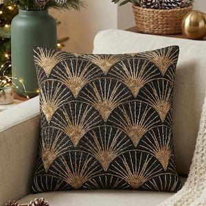 May include: A square cushion with a black and gold beaded fan design. The cushion is placed on a beige sofa. The gold beads provide a striking contrast against the black, adding a touch of elegance. The cushion measures approximately 40 cm x 40 cm.