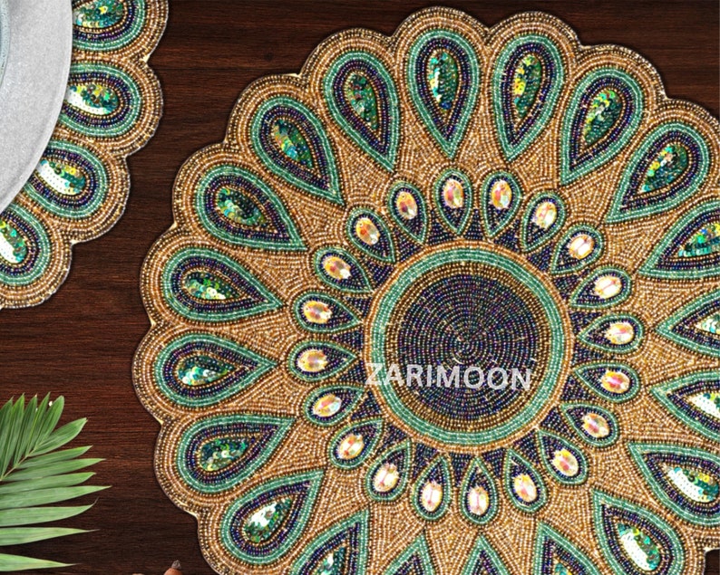 May include: A round beaded placemat with a peacock feather design. The placemat is gold with green and blue beads.