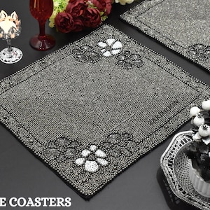 Puede incluir: Dos manteles individuales de cuentas plateadas con un diseño floral. Los manteles individuales están sobre una superficie negra. "FREE COASTERS" está escrito en blanco en la parte inferior de la imagen.