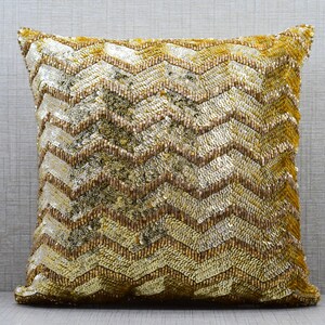 K&ouml;nnte beinhalten: Ein gold- und braunes Dekokissen mit Chevron-Muster. Das Kissen ist aus einem weichen, strukturierten Stoff.