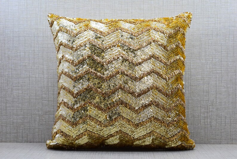 K&ouml;nnte beinhalten: Ein gold- und braunes Dekokissen mit Chevron-Muster. Das Kissen ist aus einem weichen, strukturierten Stoff.
