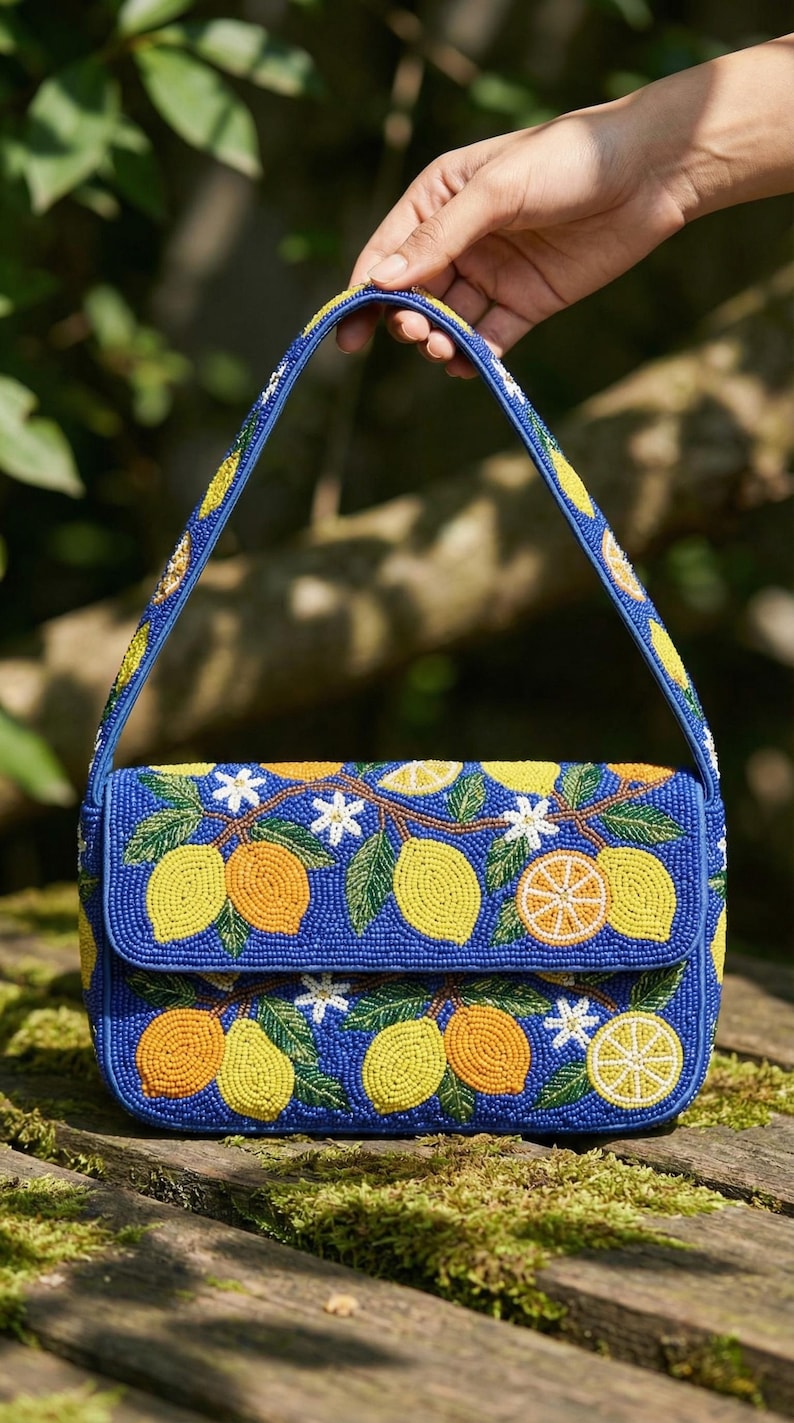 May include: A blue beaded handbag with a flap closure and a top handle. The bag is decorated with yellow lemons, orange citrus fruits, white flowers, and green leaves. The handle and the body of the bag are adorned with beads.