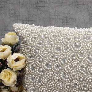 Puede incluir: Una almohada blanca con un dise&ntilde;o de perlas. La almohada est&aacute; cubierta de peque&ntilde;as perlas blancas que crean un patr&oacute;n de remolino.