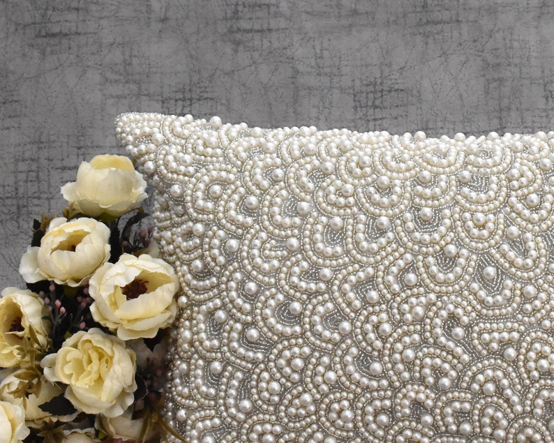 Puede incluir: Una almohada blanca con un dise&ntilde;o de perlas. La almohada est&aacute; cubierta de peque&ntilde;as perlas blancas que crean un patr&oacute;n de remolino.