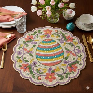 May include: A round, beige Easter placemat with a scalloped edge. The placemat features a large, colorful Easter egg design in the center, surrounded by floral and vine patterns in shades of pink, green, and purple. Gold cutlery and pink napkins are also visible.