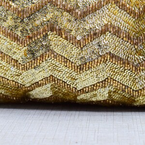 K&ouml;nnte beinhalten: Goldenes Kissen mit Pailletten und einem Chevron-Muster. Das Kissen besteht aus kleinen, gl&auml;nzenden Pailletten und Perlen.