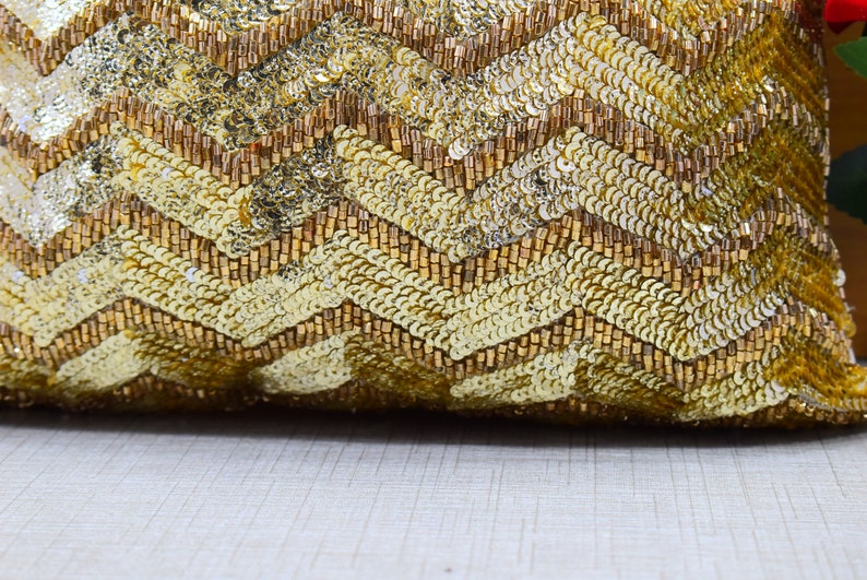 K&ouml;nnte beinhalten: Goldenes Kissen mit Pailletten und einem Chevron-Muster. Das Kissen besteht aus kleinen, gl&auml;nzenden Pailletten und Perlen.