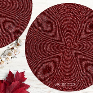 May include: Two round red beaded placemats on a white wooden surface. The placemats have a concentric circle design.